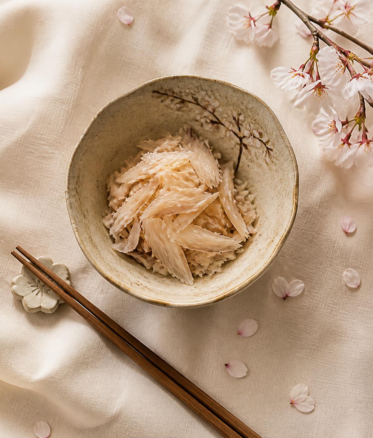 A Japanese ceramic bowl of delicate flaked fish beside cherry blossom